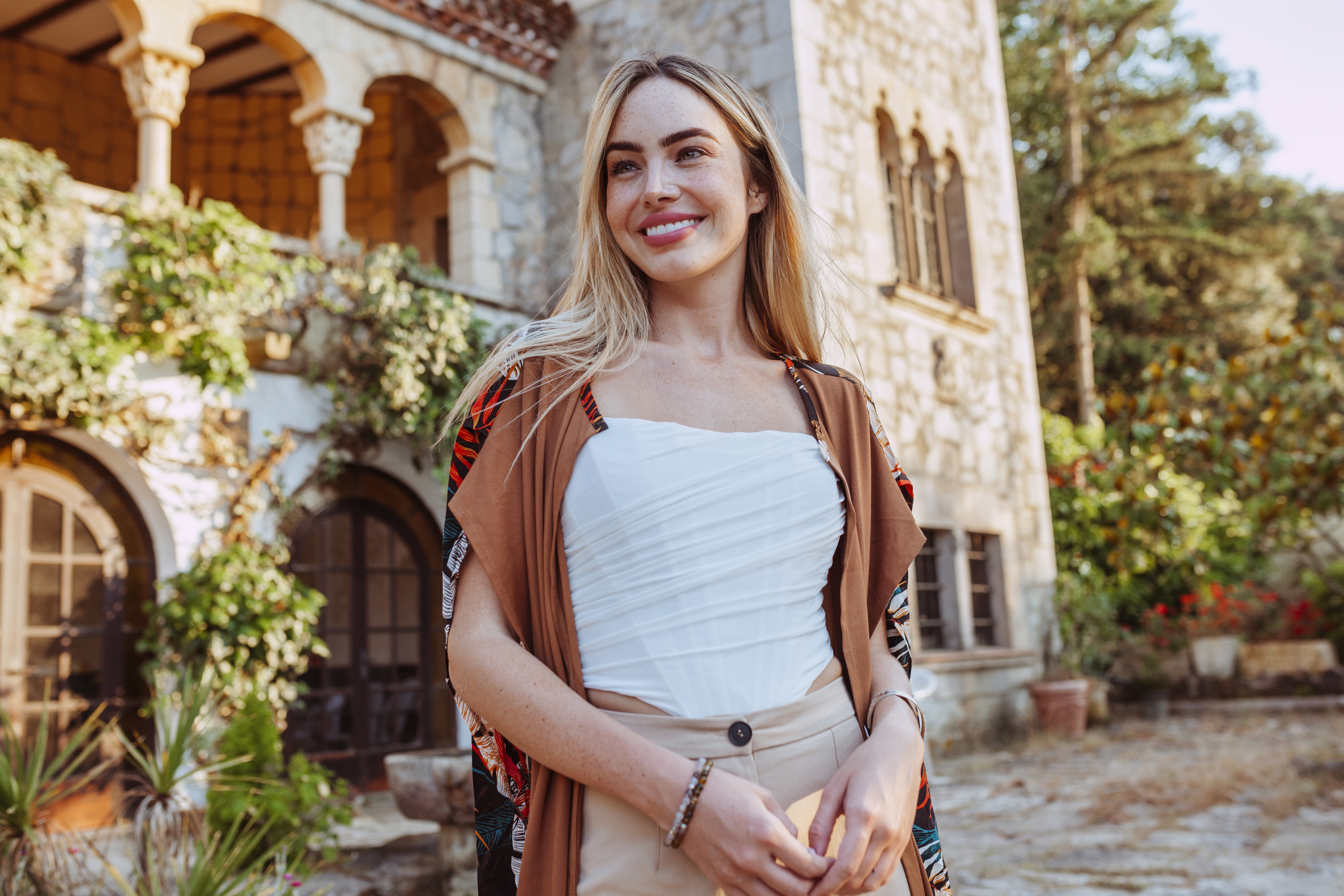 Joyful young woman smiling in front of a beautiful villa, showcasing a radiant and healthy smile from Princeton Prosthodontics
