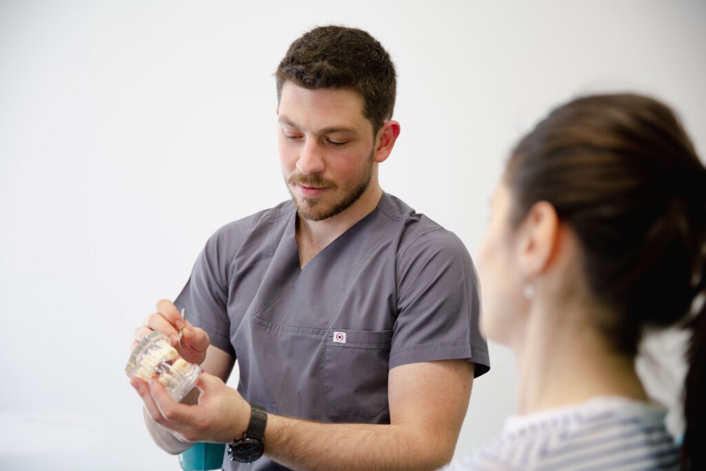 Dentist explaining a dental implant restoration using a tooth model during a patient consultation.